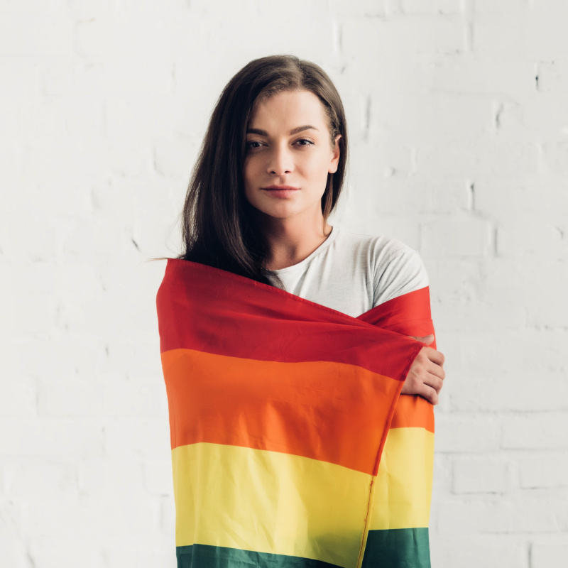 Transgender young adult wrapped in a rainbow pride flag.