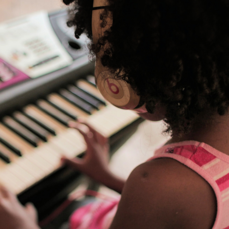 A young person playing a keyboard with a pair of Beats headphones.